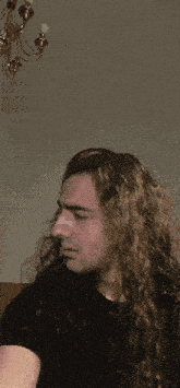 a man with long curly hair and a black shirt looks down