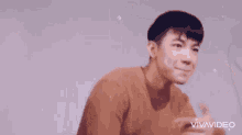 a man wearing an orange sweater is standing with his hands on his hips .