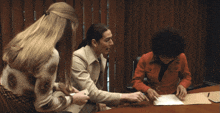 a woman in a red jacket sits at a table talking to two other women
