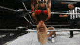 a woman is hanging upside down in a wrestling ring while a referee looks on .