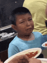 a young boy in a blue shirt is crying while holding a plate of food