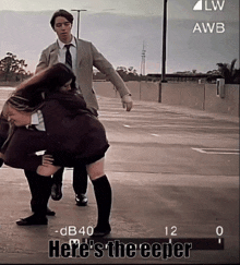 a man in a suit and tie is holding a woman in a parking lot with the words here 's the creeper on the screen