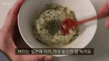 a person is mixing a sauce in a bowl with a red spoon .