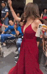 a woman in a red dress is dancing in front of a crowd of people while holding a cell phone .