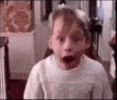 a young boy is making a funny face with his mouth open in a hallway .