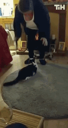 a black and white cat is playing with a man in a living room with the letters th on the bottom