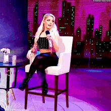 a woman is sitting in a chair holding a microphone in front of a city skyline .