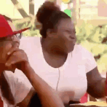 a man and a woman are sitting at a table eating food . the woman is wearing a red hat and glasses .