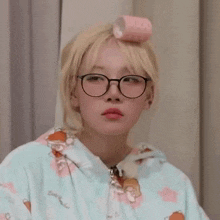 a woman wearing glasses and a hoodie has a pink curling iron on her head .