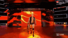 a wrestler is walking on a stage with a large screen behind him that says w live
