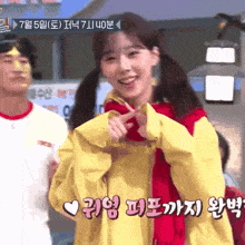 a girl in a yellow jacket and red scarf is smiling and making a heart shape with her hands