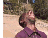 a man in a purple shirt is laughing with his mouth wide open .