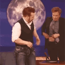 two men are standing in front of a full moon and one is taking off his shirt
