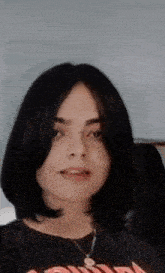 a young girl with short black hair is wearing a black shirt and a necklace .