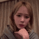 a young woman with blonde hair is making a funny face while holding her hand to her chin .