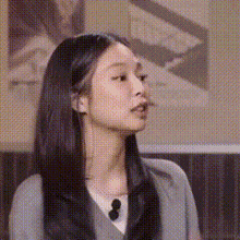 a woman with long black hair is wearing a gray sweater and a black tie .