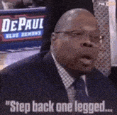 a man in a suit and tie is standing in front of a sign that says ' depaul blue demons ' on it .