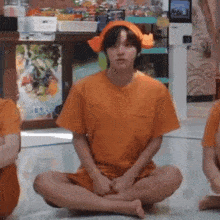 a man in an orange shirt is sitting on the floor .