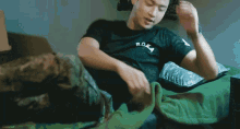 a man in a black t-shirt is laying on a green blanket
