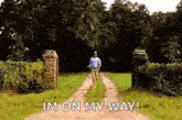 a man is walking down a dirt road with the words `` i 'm on my way '' written on it .