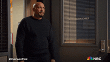 a man in a black shirt stands in front of a window that says " chief " on it
