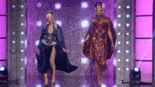two drag queens are walking down a runway in front of purple lights