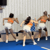 three cheerleaders are dancing on a blue mat in front of a wall .