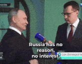 a man in a suit and tie is talking into a microphone while another man says russia has no reason and no interest