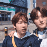 two young men are taking a selfie in front of a building that says ' 하나은행 ' on it