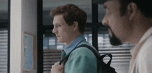 a man with a backpack is walking next to another man in a hallway .