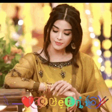 a woman in a yellow dress is sitting at a table with her hands on her wrists .