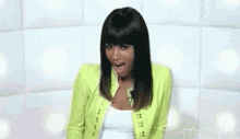 a woman in a green jacket is sitting on a white couch smiling .