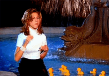 a woman in a white turtleneck stands in front of a fountain with rubber ducks in it