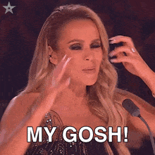 a woman says " my gosh " in front of a microphone with her hands in the air