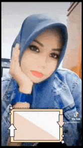 a woman wearing a blue hijab and a denim jacket is taking a selfie .