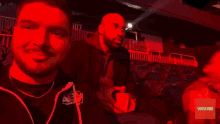 two men are standing in a dark room with a subscribe button on the bottom right