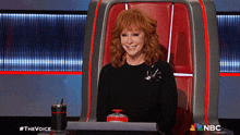 a woman with red hair is sitting in a chair with a nbc logo on it