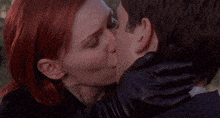 a man and a woman are kissing in a park . the woman has red hair .