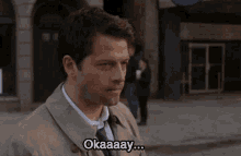 a man in a suit and tie says okaaay in front of a building