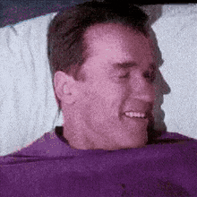 a man in a purple shirt is smiling while laying in bed