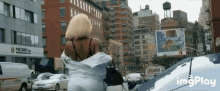 a gif of a woman walking down a city street with the words imgplay in the lower right corner