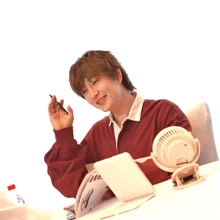 a person sitting at a desk with a fan and a book