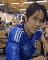 a young man wearing a blue and white adidas shirt is sitting at a table .