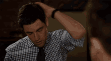 a man in a plaid shirt and tie holds his hand to his head