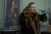 a man in a fur coat stands in front of a painting of a man