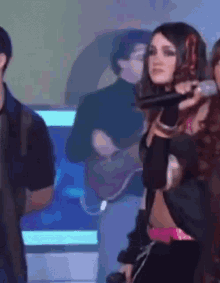 a woman is singing into a microphone while a man plays a guitar in the background