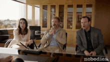 a group of people sitting at a table with the word nobodies on the bottom right