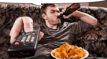 a man sitting on a couch holding a remote control and a bottle of beer