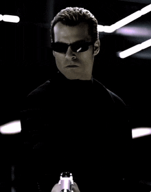 a man in a black suit and sunglasses holds a gun