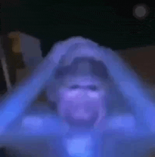 a man is sitting in a dark room with his hands on his head and a blue light behind him .